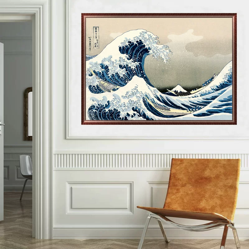 Framed artwork of a wave painting on a wall with a chair in the foreground.
