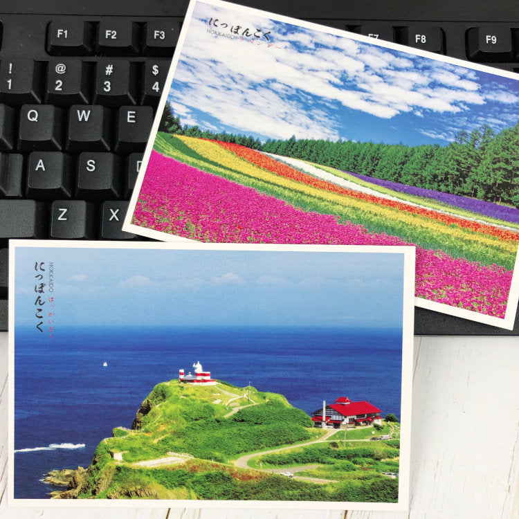 Two scenic postcards on a keyboard, one with a colorful field and the other with a coastal view.