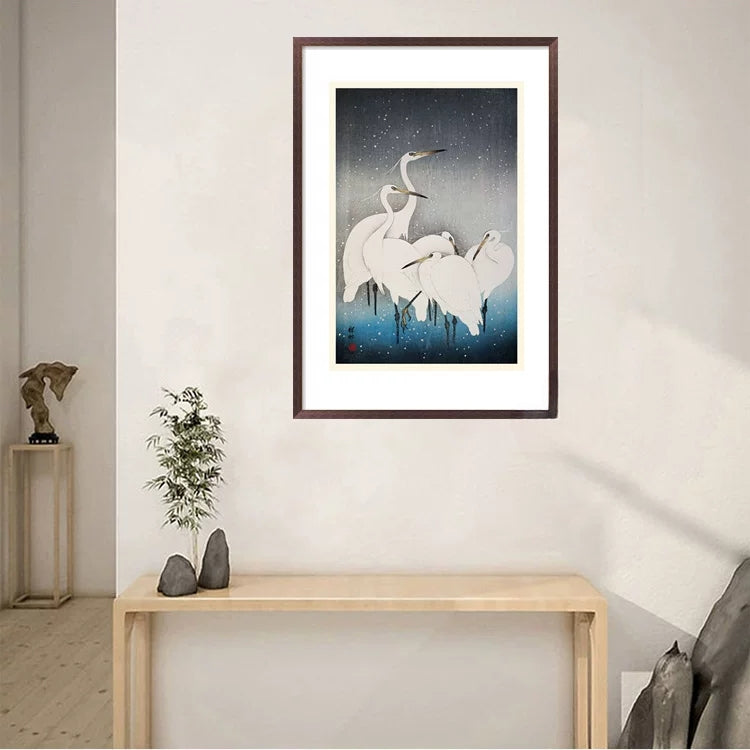 Framed artwork of cranes on a wall above a wooden console table.