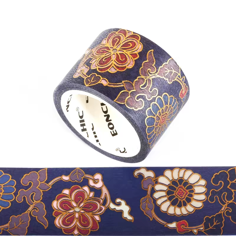 A roll of decorative washi tape with a navy blue background and traditional floral patterns outlined in gold, with some flowers filled in red and cream. A strip of the tape is shown unrolled below the main roll on a white background.