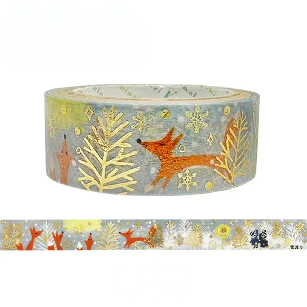 A roll of decorative washi tape with a winter forest pattern, featuring orange foxes, gold trees, and snowflakes on a muted blue-gray background, shown with a strip unrolled below on a white background.