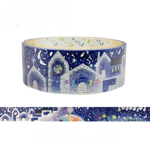 A roll of decorative washi tape featuring a winter night village scene with snow-covered houses, stars, and moons on a dark blue background, shown with a strip unrolled below on a white background.