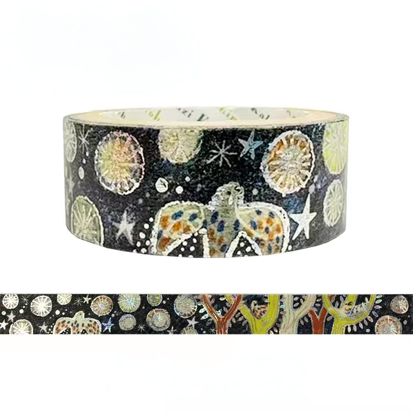 A roll of decorative washi tape with a black background and a whimsical pattern of stars, moons, and abstract butterfly-like figures in muted green, beige, blue, and orange. A strip of the tape is shown horizontally below the roll on a plain white background.