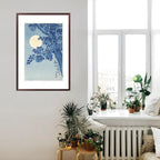 Framed artwork of a blue tree with a moon on a white wall in a room with plants and a window.