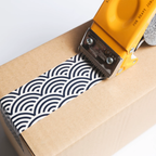 Sealant gun applying black and white patterned tape to a cardboard box.