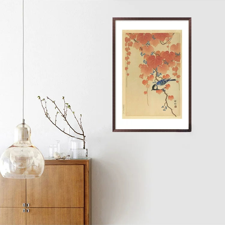 Framed artwork of a bird and flowers on a wall above a wooden cabinet.
