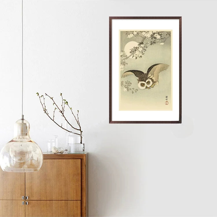 Framed artwork of an owl with cherry blossoms on a wall above a wooden cabinet.